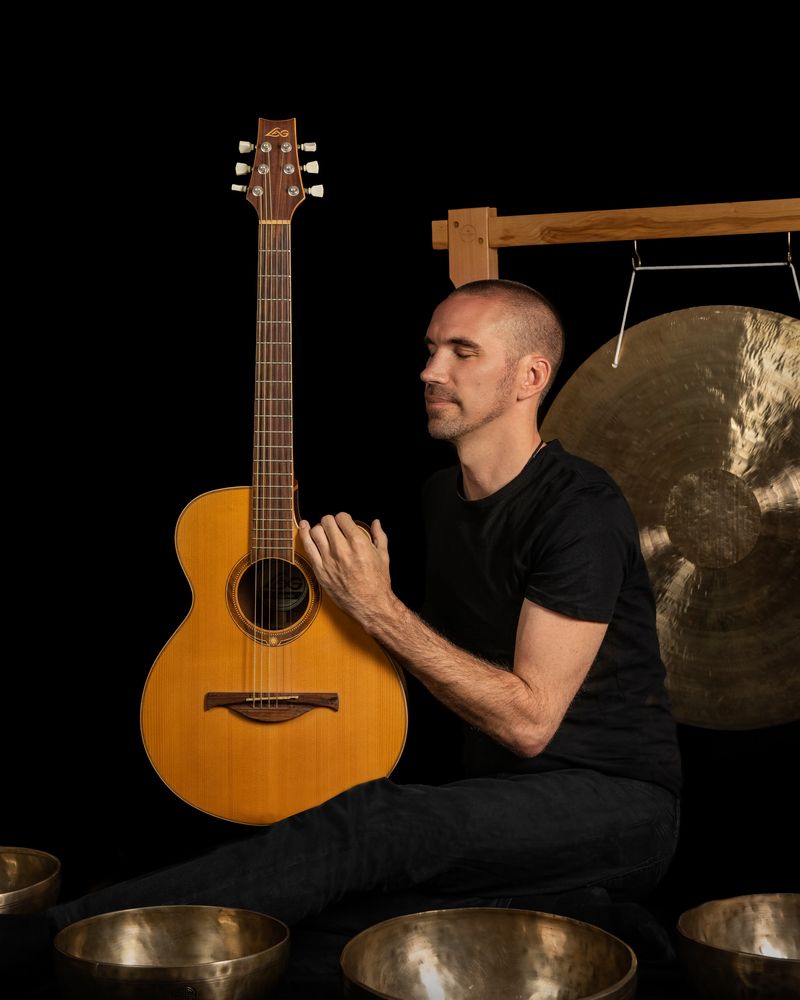 Jorn Ayan with acoustic guitar, singing bowls and gong on a black background