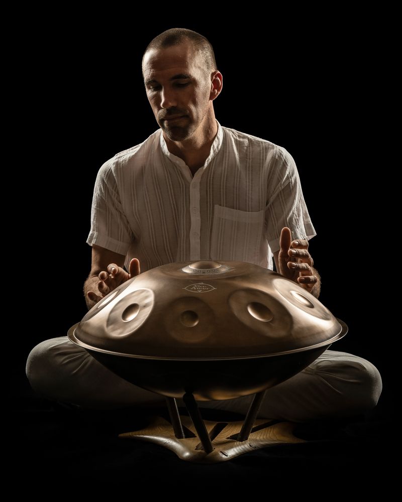Jorn Ayan playing handpan, lit against a black background