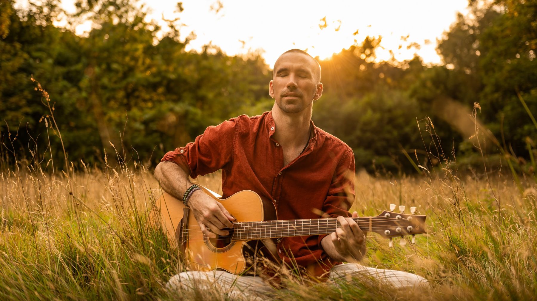 Jorn Ayan playing guitar in a meadow at sunset