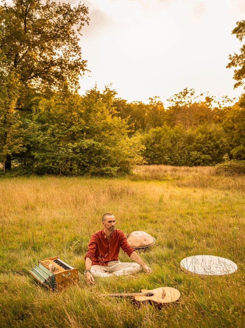 Jorn Ayan seated in a meadow surrounded by his instruments