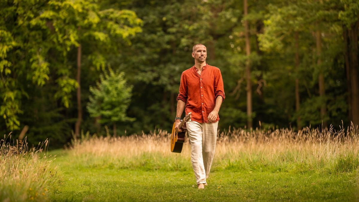 Jorn Ayan walking across a meadow carrying a guitar case